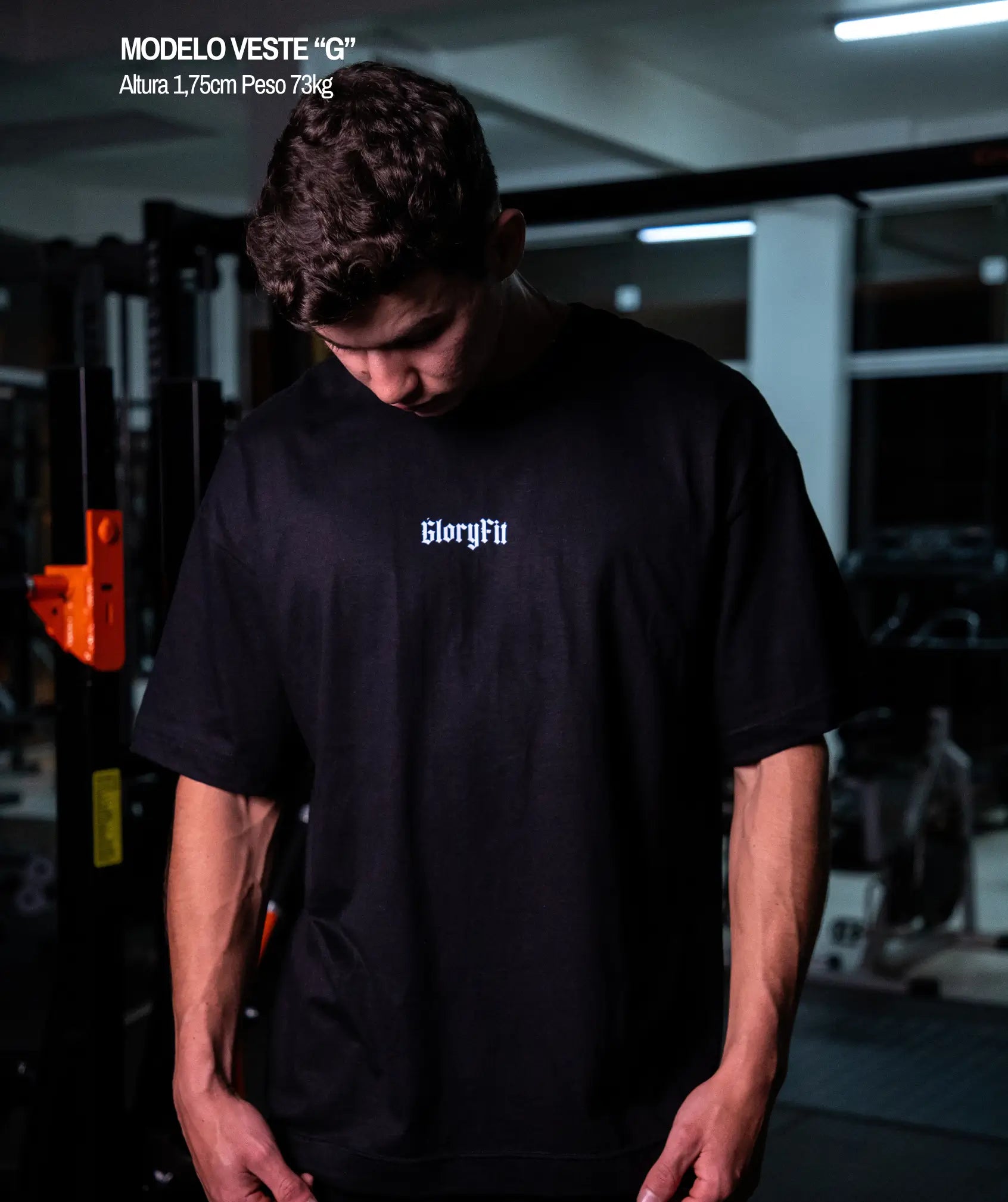 “Camiseta oversized Revelation GLORYFIT preta vista frontal com modelo em ambiente de academia