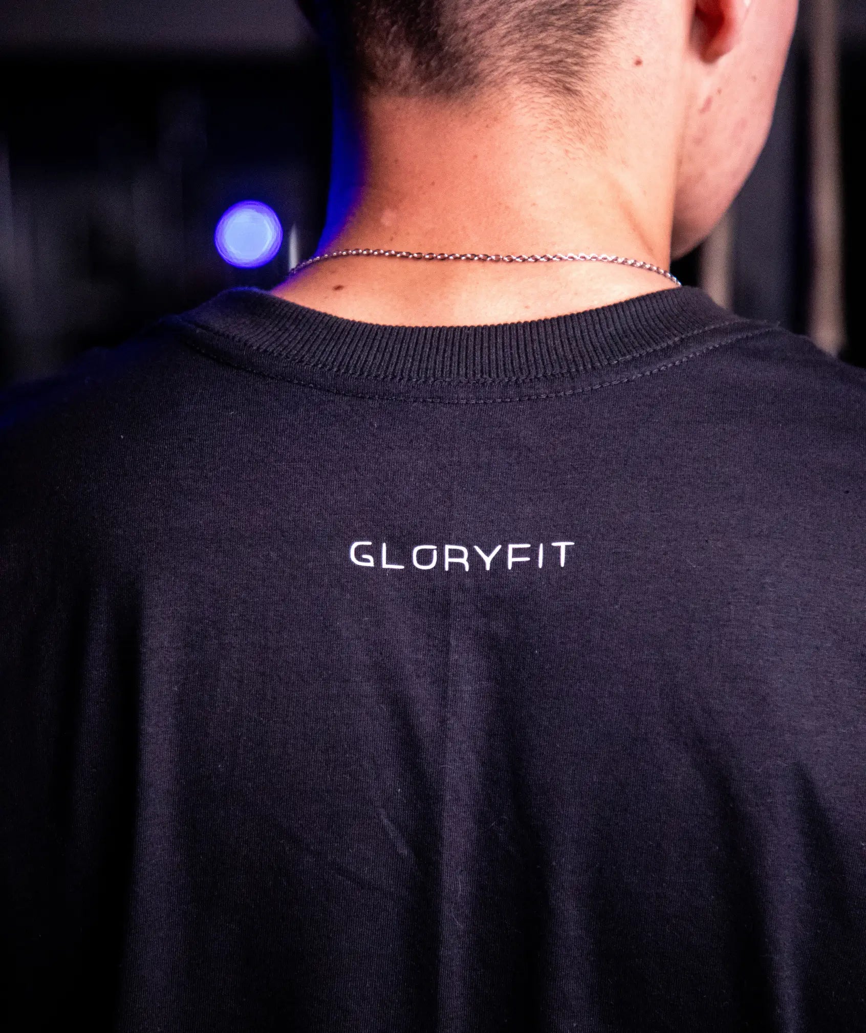 Camiseta oversized GLORYFIT preta vista traseira em ambiente de academia