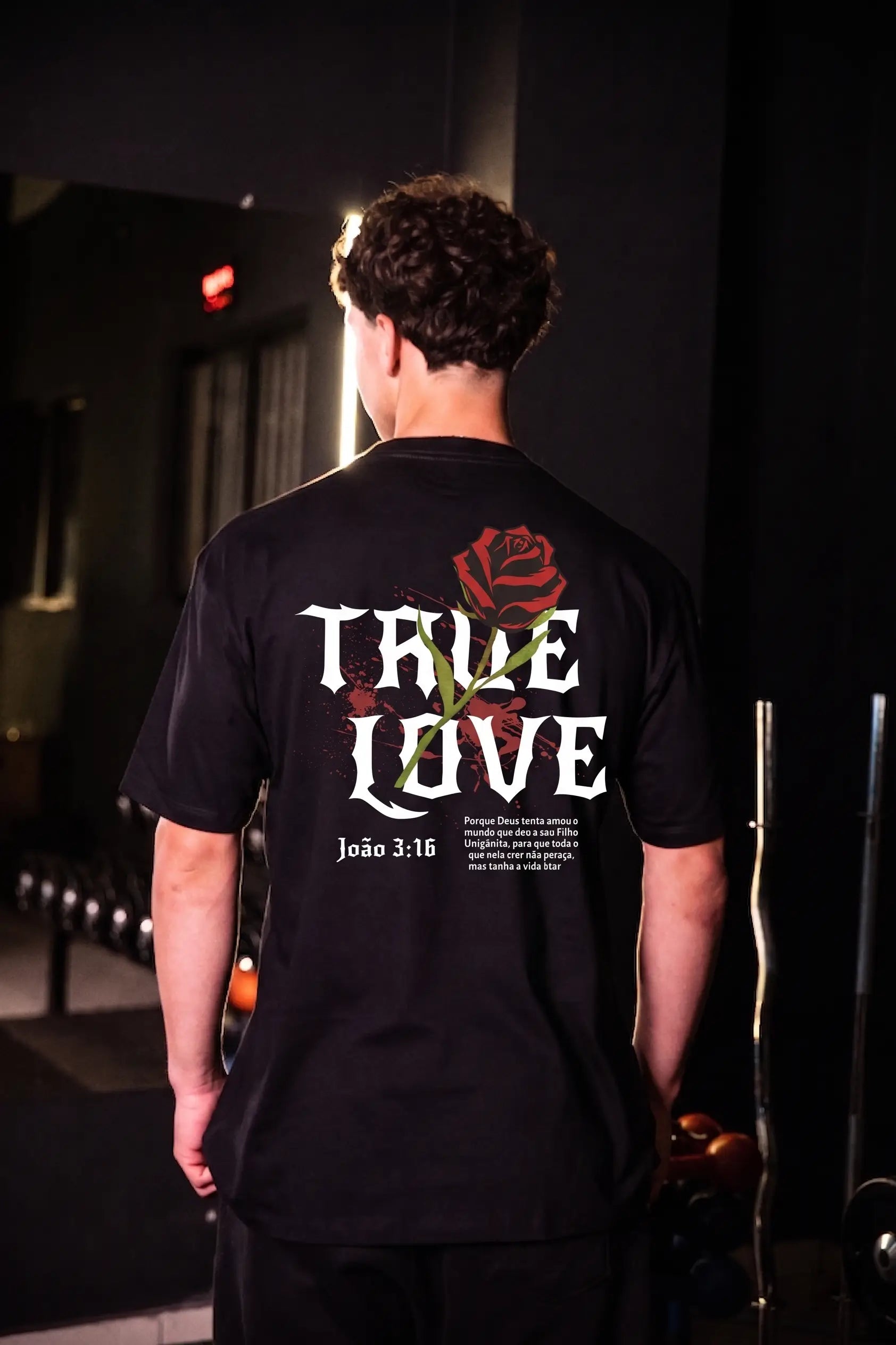 Modelo usando camiseta oversized preta True Love com rosa vermelha nas costas e versículo João 3:16